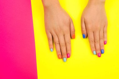 Parlak arkaplanda neon renkleri olan mükemmel manikürlü kadın elleri.