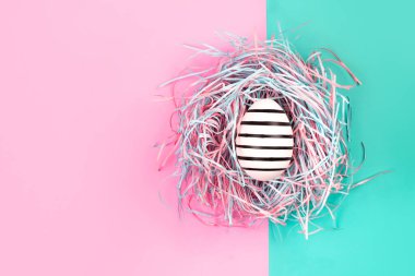 Mavi ve pembe pastel arka planda dekoratif yuvada elle boyanmış yumurta. Paskalya konsepti.