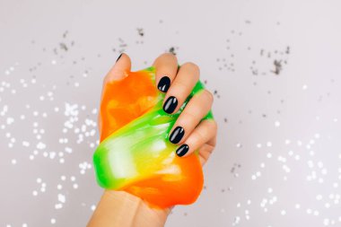 Turuncu ve yeşil renkli balçık tutan siyah manikürlü eller.