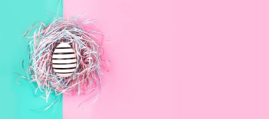 Mavi ve pembe pastel arka planda dekoratif yuvada elle boyanmış yumurta. Paskalya konsepti.