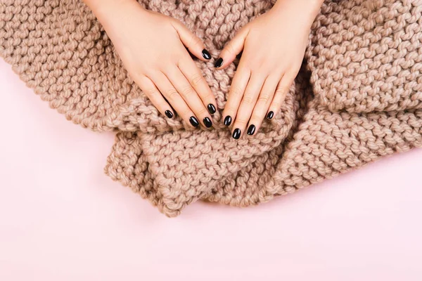 Black manicure with cozy wool knitted scarf on pastel background. — Stock Photo, Image