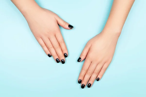 Womans hands with black manicure on silver circle and pastel blue background. — ストック写真