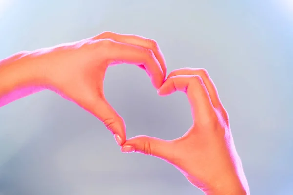 Young womans hands made gesture of heart shape in trendy neon light. — Stock Photo, Image
