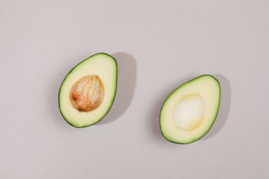 Avokadonun iki parçası. Gri arkaplanda düz uzanma biçimi.