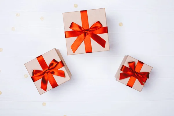 Three present boxes with red bow on white wooden background with golden confetti. Flat lay, place for text.