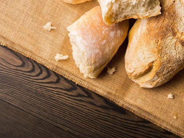 Frissen sült kenyeret, zsákvászon sötét fából készült háttér — Stock Fotó