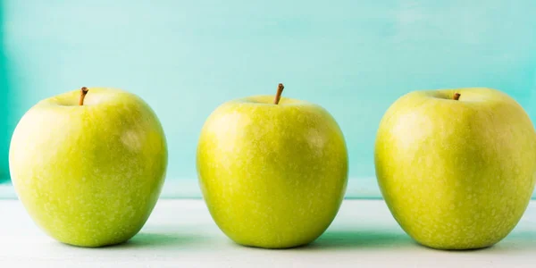 Drei grüne Äpfel auf türkisfarbenem Hintergrund — Stockfoto
