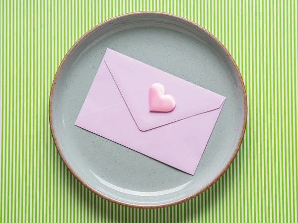 Gray dish with pink envelope on green — Stock Photo, Image