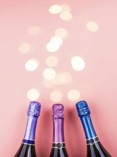 Três garrafas de champanhe e luzes bokeh em rosa — Fotografia de Stock