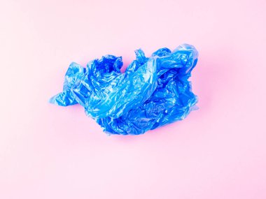 Pembe arka planda buruşmuş mavi plastik çöp torbası.