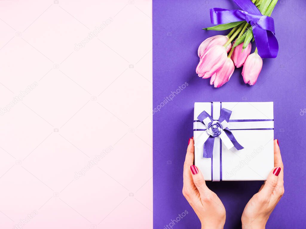 Female hand with gift and tulips on purple pink