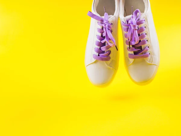 White sneakers with purple laces on yellow background