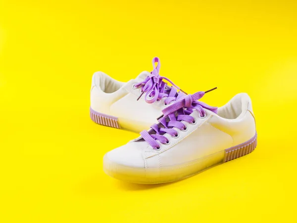 White sneakers with purple laces on yellow background