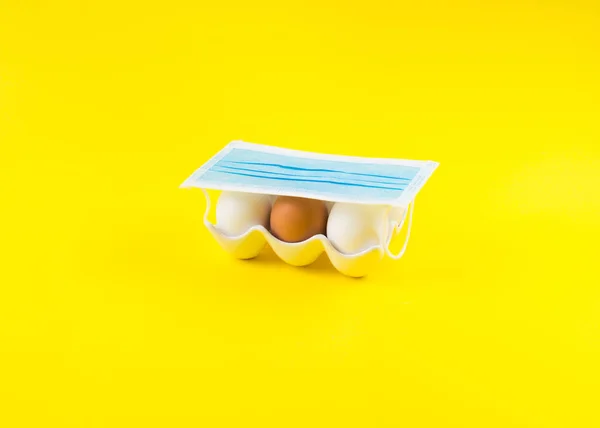 Blanco y un huevo marrón en amarillo debajo de la máscara facial — Foto de Stock