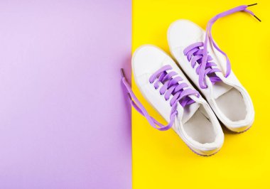 Sarı arka planda mor bağcıklı beyaz spor ayakkabılar.