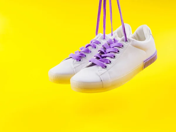 White sneakers with purple laces on yellow background