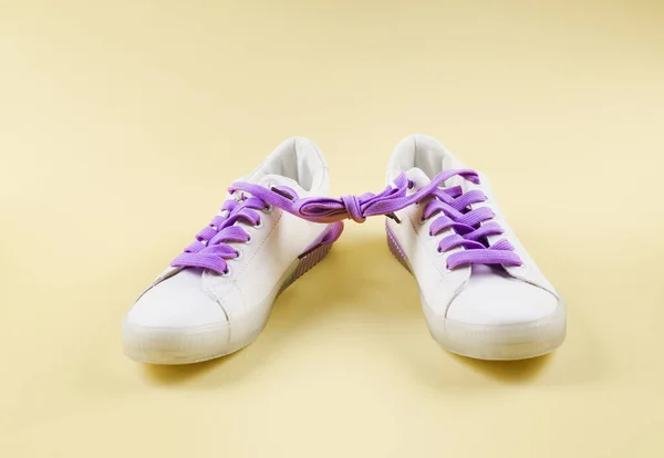 White sneakers with tied purple laces on beige