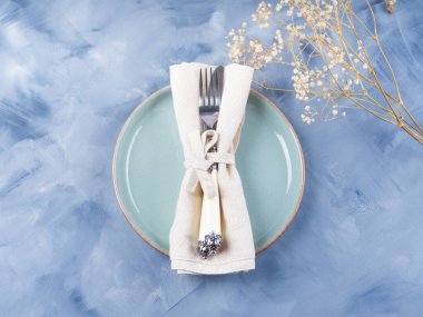 Mavi pastel tabak ve kurumuş çiçekli çatal bıçak takımı.