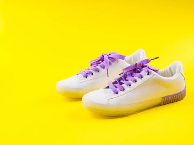Sarı arka planda mor bağcıklı beyaz spor ayakkabılar.
