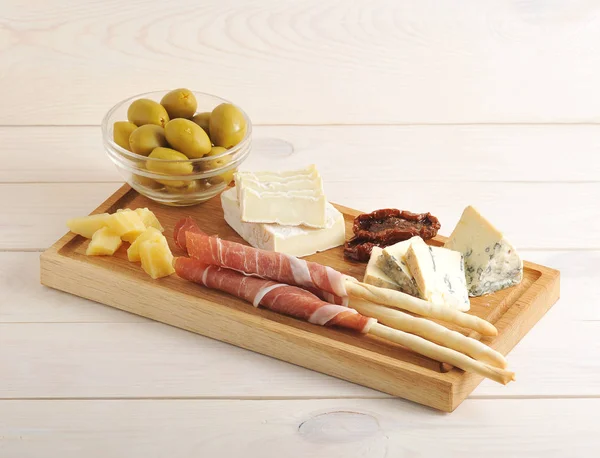 Bacon on bread sticks, cheese, dried tomatoes, olives on a woode — Stock Photo, Image