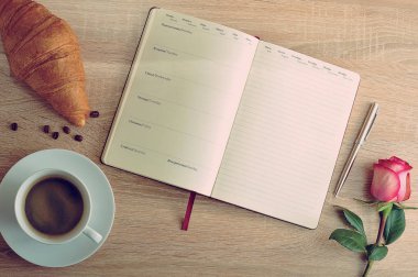 kırmızı gül ve bir fincan kahve ile bir kruvasan ve gün ile günlüğü