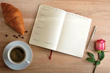 kırmızı gül ve bir fincan kahve ile bir kruvasan ve gün ile günlüğü