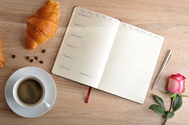 kırmızı gül ve bir fincan kahve ile bir kruvasan ve gün ile günlüğü