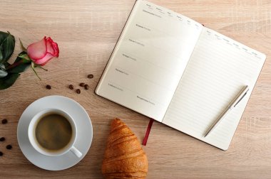 kırmızı gül ve bir fincan kahve ile bir kruvasan ve gün ile günlüğü