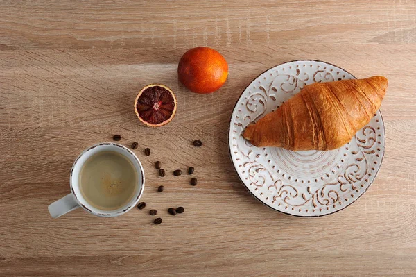 Croissant on a plate with a Cup of coffee and red blood orange — Stock Photo, Image