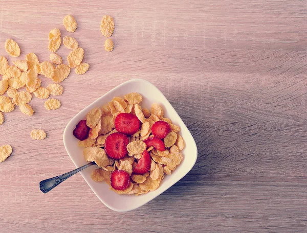 Cornflakes with strawberries on wooden background — Stock Photo, Image