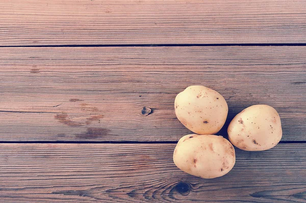 Três jovens tubérculo cru batatas brancas no fundo de madeira rústica — Fotografia de Stock