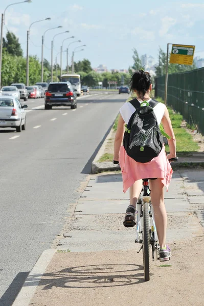 Meisje rijdt een fiets langs een drukke snelweg - achteraanzicht — Stockfoto