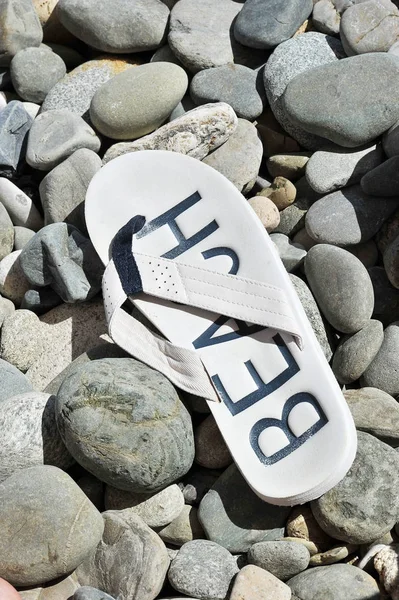 Chinelos brancos com a palavra praia na praia de seixos — Fotografia de Stock