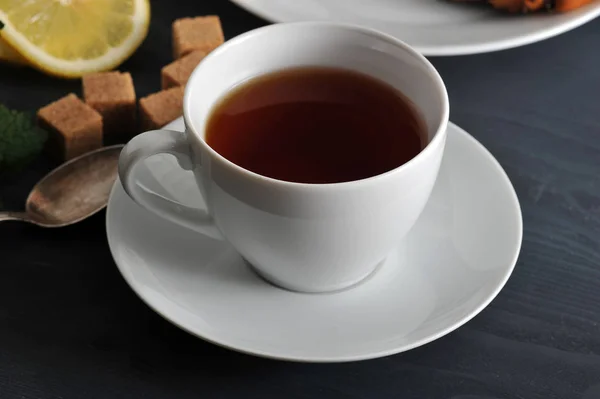 Μαύρο τσάι σε μια κούπα σε ένα πιατάκι, λεμόνι και δυόσμο — Φωτογραφία Αρχείου