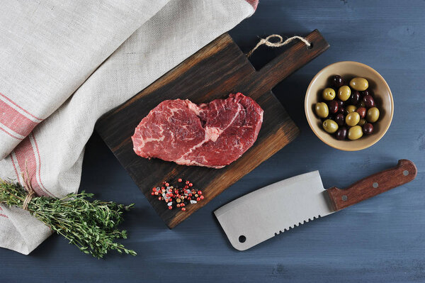 piece of beef on a wooden Board, a knife for meat, olives and th