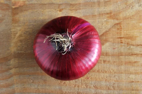 Una cebolla entera en rojo sobre fondo de madera áspera —  Fotos de Stock