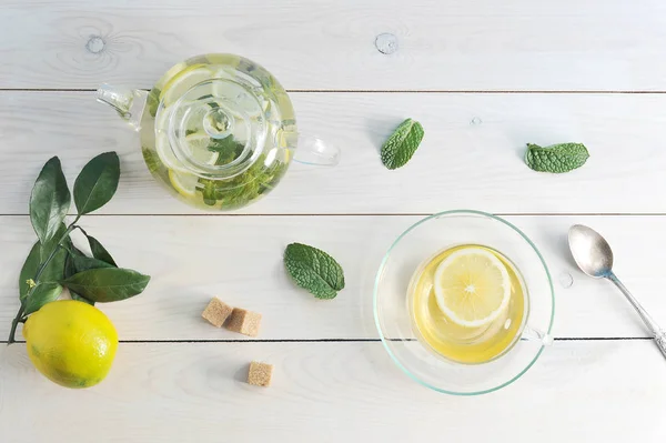 Чай с лимоном и мятой в стеклянной чашке, чайник и чайная ложка на WH — стоковое фото