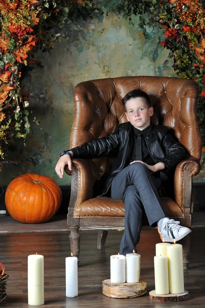 Niño de 10 años en una chaqueta de cuero se sienta en una silla de cuero — Foto de Stock