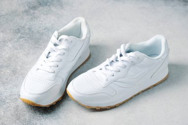 Gri arka planda bir çift beyaz spor ayakkabı.