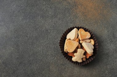 Gri arka planda kağıt bir sepetin içinde kalp şeklinde ev yapımı kurabiyeler ve figürler.