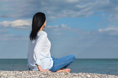 Beyaz saçlı, orta yaşlı, gökyüzüne bakan, kumsalda dinlenen, geleceği düşünen bekar bir kadın.