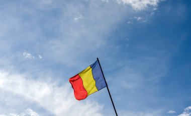 Romanya bayrağının düşük açılı görüntüsü bulutlu mavi gökyüzünü kaplıyor.