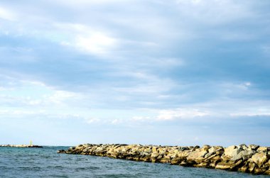 Taşlar dalgalanıyor dalgalar dalgalanıyor ve deniz mavi gökyüzüne karşı .
