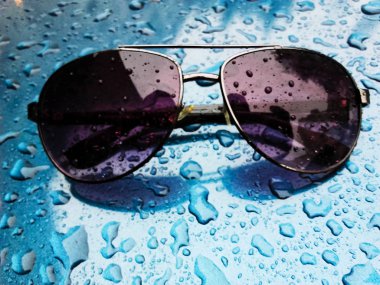 Mavi arka planda yağmur damlalarıyla kaplı güneş gözlükleri