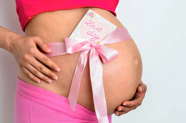 Zijaanzicht middendoorsnede van blanke zwangere jonge vrouwen met een laatste dag geschreven hangende stok notities op de buik staande tegen witte achtergrond — Stockfoto