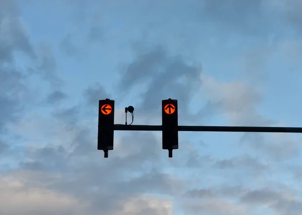 Visão de baixo ângulo dos semáforos vermelhos com a seta apontando para a frente e para a esquerda contra o céu azul nublado  . — Fotografia de Stock