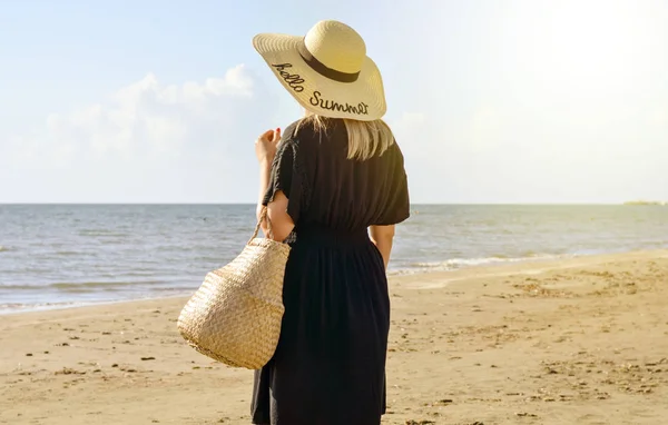 Elinde hasır şapka ve sepetle plajda dinlenen bekar bir kızın arka görüntüsü. Parlak ılık filtre .