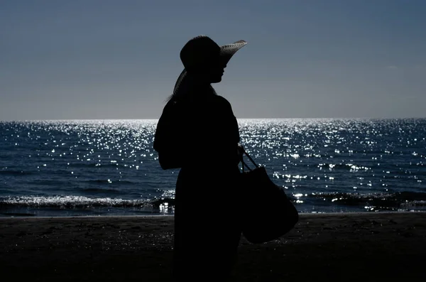  Hasır şapkalı, elinde sepeti olan ve sabahın erken saatlerinde denize bakan kadın silueti. Yunanistan yaz tatili .