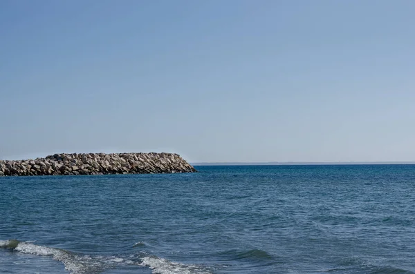 Yazın mavi gökyüzüne karşı taşların dalga kıran ve denizin yan görüntüsü . — Stok fotoğraf