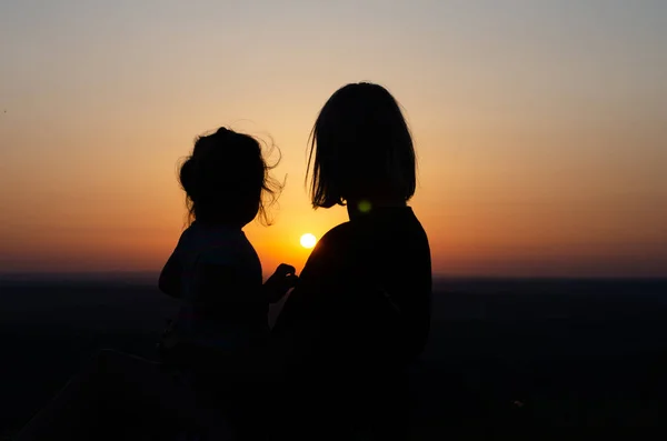 Mother and daughter who sit and look at the sunset . — Stock Photo, Image